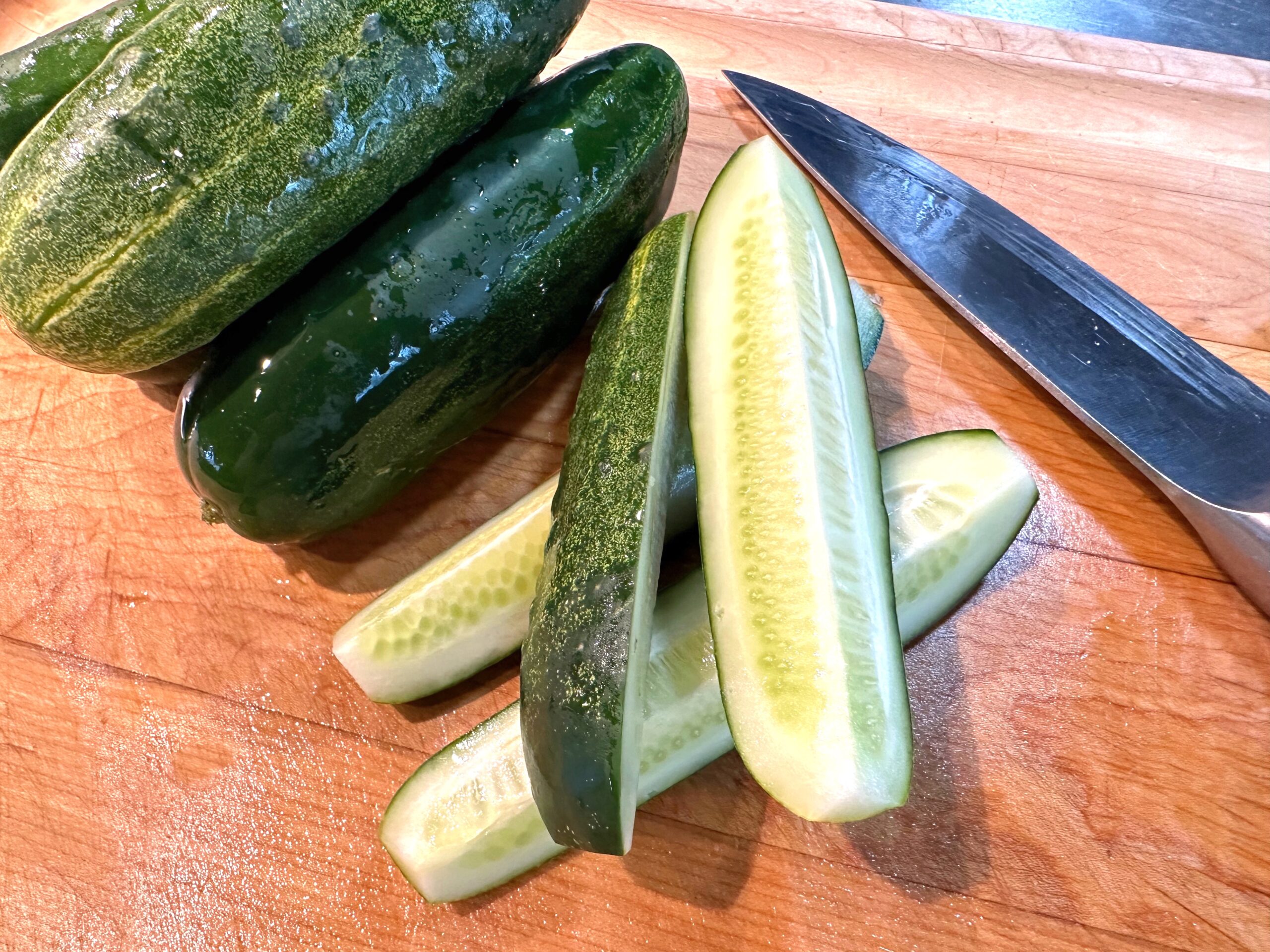 Kirby cucumbers sliced on a cutting board with knife